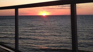 Un coucher de soleil sur l’océan, vu depuis un balcon doté d’une rambarde en métal.