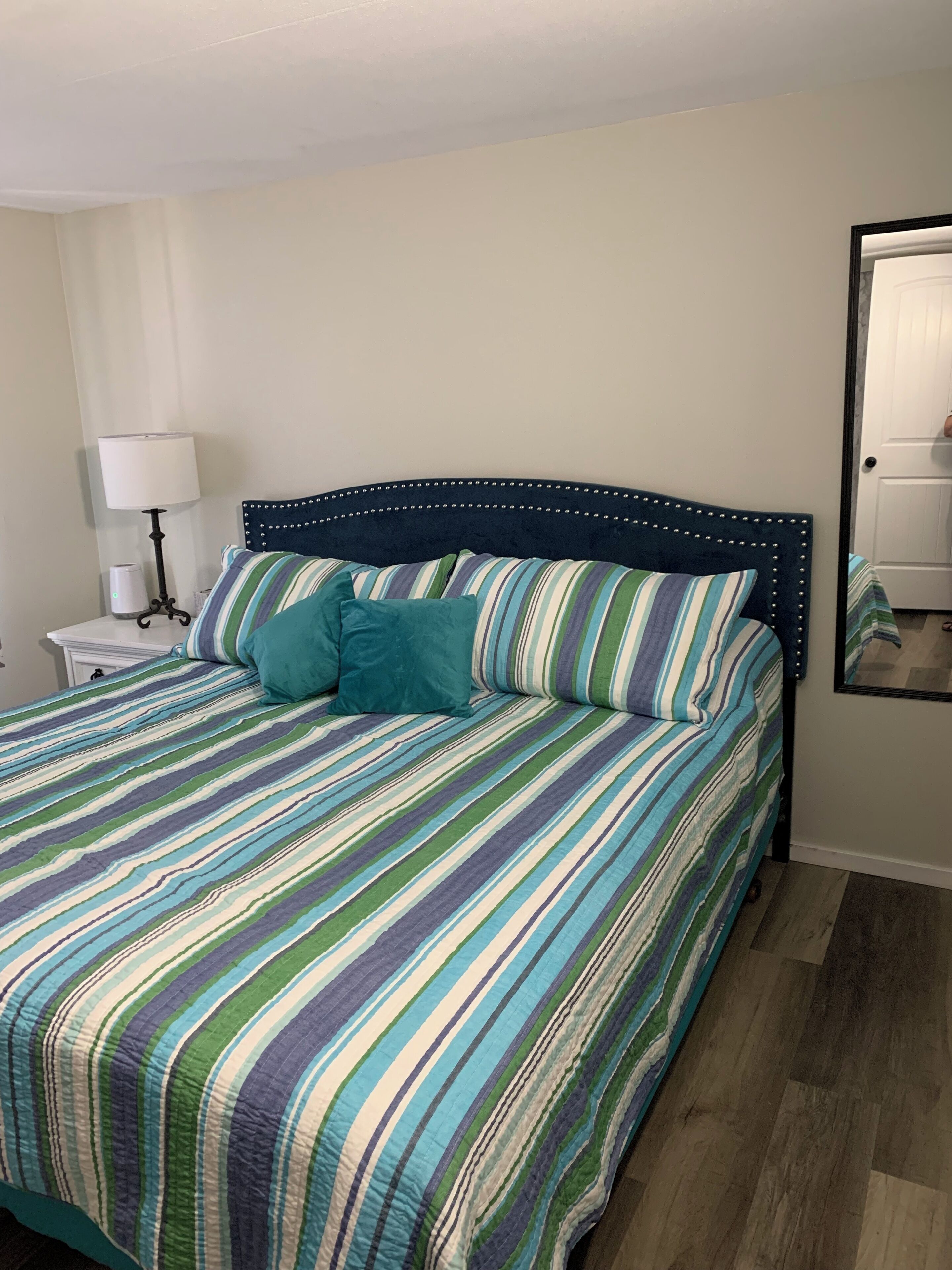 Uma cama com colcha listrada, um travesseiro azul-turquesa e cabeceira com padrão decorativo.
