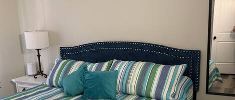 Uma cama com colcha listrada, um travesseiro azul-turquesa e cabeceira com padrão decorativo.