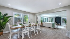 A spacious living area with a dining table, white chairs, and a sofa.