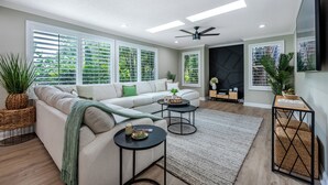 A modern living room with a sectional sofa, two round coffee tables, and a large window with blinds.