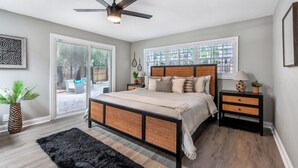 A bedroom with a bed, a ceiling fan, a nightstand, a potted plant, and a window with blinds.