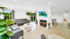 A modern living room with a grey sofa, a round coffee table, a fireplace, and a TV mounted above it.