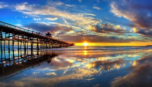 Um píer se estendendo para o oceano, com o pôr do sol ao fundo.