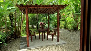 Un kiosque en bois doté d’un sol carrelé, entouré d’une végétation luxuriante et de bananiers.
