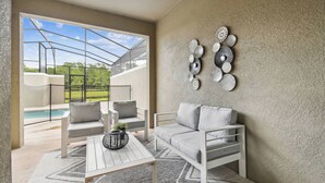 A modern outdoor seating area with a pool, white furniture, and decorative wall art. - Luxury 4BR Townhome w/ Pool Near Disney (Kissimmee)