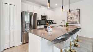 A modern kitchen with white cabinets, stainless steel appliances, and a central island with bar stools. - Luxury 4BR Townhome w/ Pool Near Disney (Kissimmee)