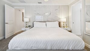 A large, neatly made bed with a white bedspread in a hotel room with marble walls, two bedside tables with lamps, and a chandelier. - Luxury 4BR Townhome w/ Pool Near Disney (Kissimmee)