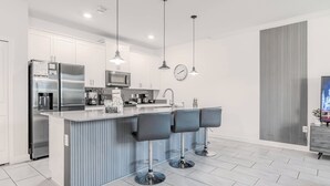 A modern kitchen with a central island, stainless steel appliances, pendant lighting, and a bar area with stools.