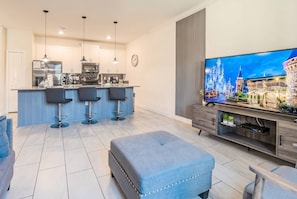 A modern kitchen with a central island, bar stools, a flat-screen TV, and a large window. - Comfortable 4BR Home with Pool at Storey Lake (Kissimmee)