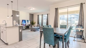 A modern kitchen with a dining area, a TV, and a balcony with curtains.