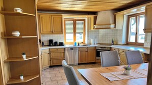 A modern kitchen with wooden cabinets, a dishwasher, a stove, and a dining area with a table and chairs. - ~straubings Großes Apartment~ (Straßkirchen)