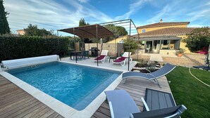 Una piscina con bordo in legno, lettini e una zona patio coperta.