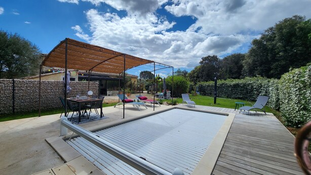 Un'area esterna riparata con piscina, poltrone relax e un tavolo.