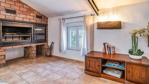 A living room with a brick fireplace, a window with curtains, a wooden cabinet with books, and a potted plant. - Stunning home in Torrox (Torrox)