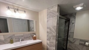 A modern bathroom with a large mirror, a sink with a faucet, a wooden vanity, and a shower area with glass doors. - Centrally located home in the heart of Twin Falls.  (Twin Falls)