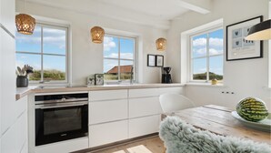 A modern kitchen with white cabinetry, a built-in oven, and a large window overlooking a grassy area. - 2 bedroom stunning home in Blåvand (Blåvand)
