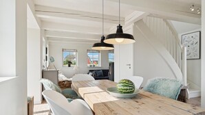 A spacious dining area with a wooden table, white chairs, and a large watermelon centerpiece. - 2 bedroom stunning home in Blåvand (Blåvand)