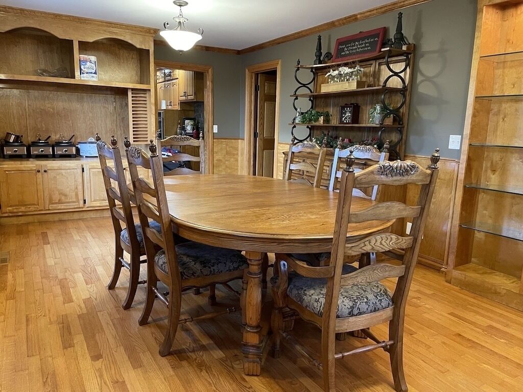 Un coin repas avec une table et des chaises en bois, une cuisine avec des meubles en bois et une étagère décorative où sont exposés des objets en verre.