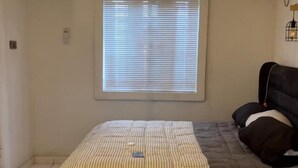 Un dormitorio con cama, ventana con persianas, lámpara colgante y un equipo de aire acondicionado en la pared.