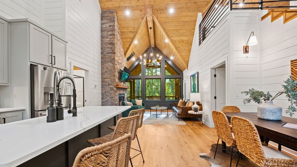 A spacious kitchen with a central island, a dining area with wicker chairs, and a cozy seating area with a fireplace. - Lazy Day Hideaway Cabin | Modern-Boho Retreat (Broken Bow)