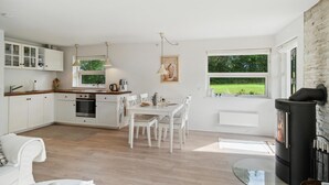 A modern kitchen with white cabinetry, a dining area with white chairs, and a large window offering a view of a green landscape.