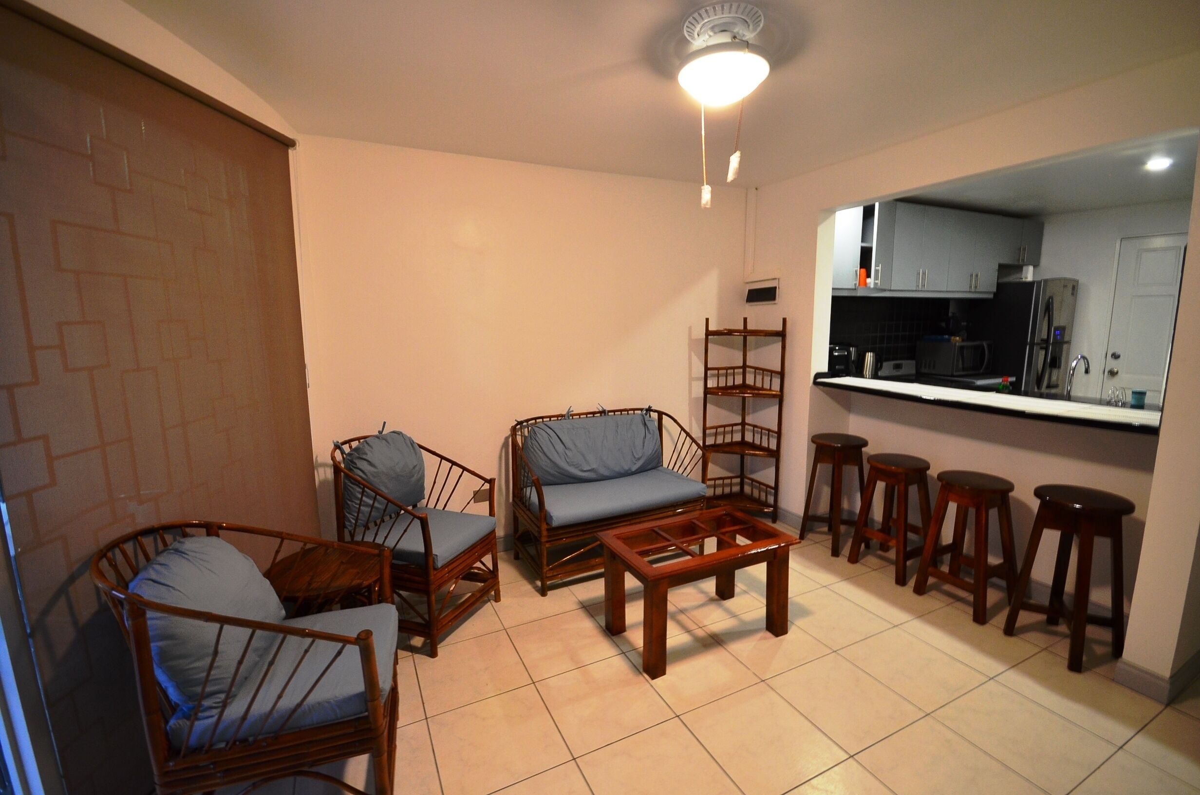 A compact living space with a kitchenette, two wooden chairs with cushions, a wooden coffee table, and a bar stool line.