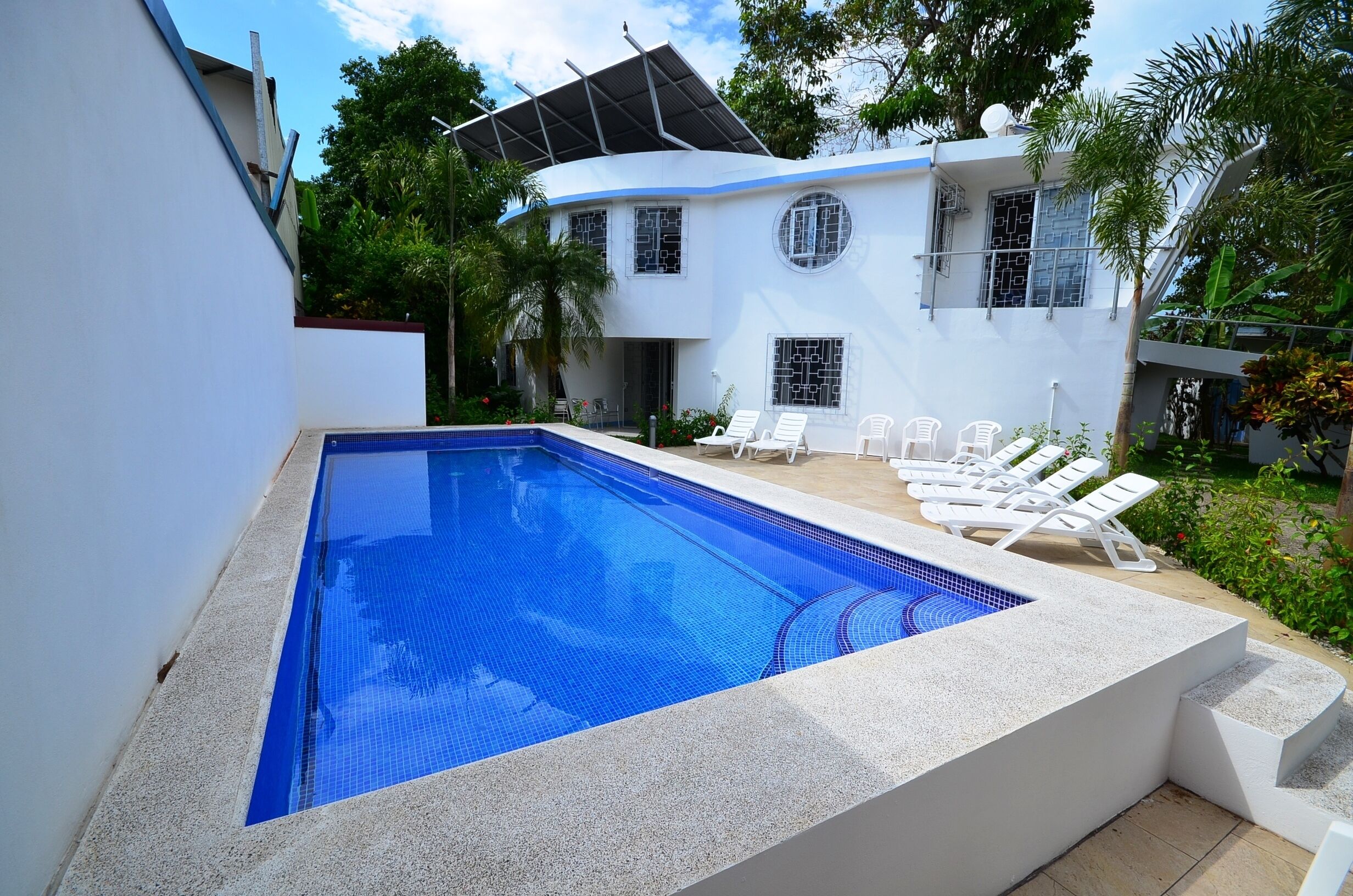 A modern house with a swimming pool, white exterior, and a covered patio area with lounge chairs.