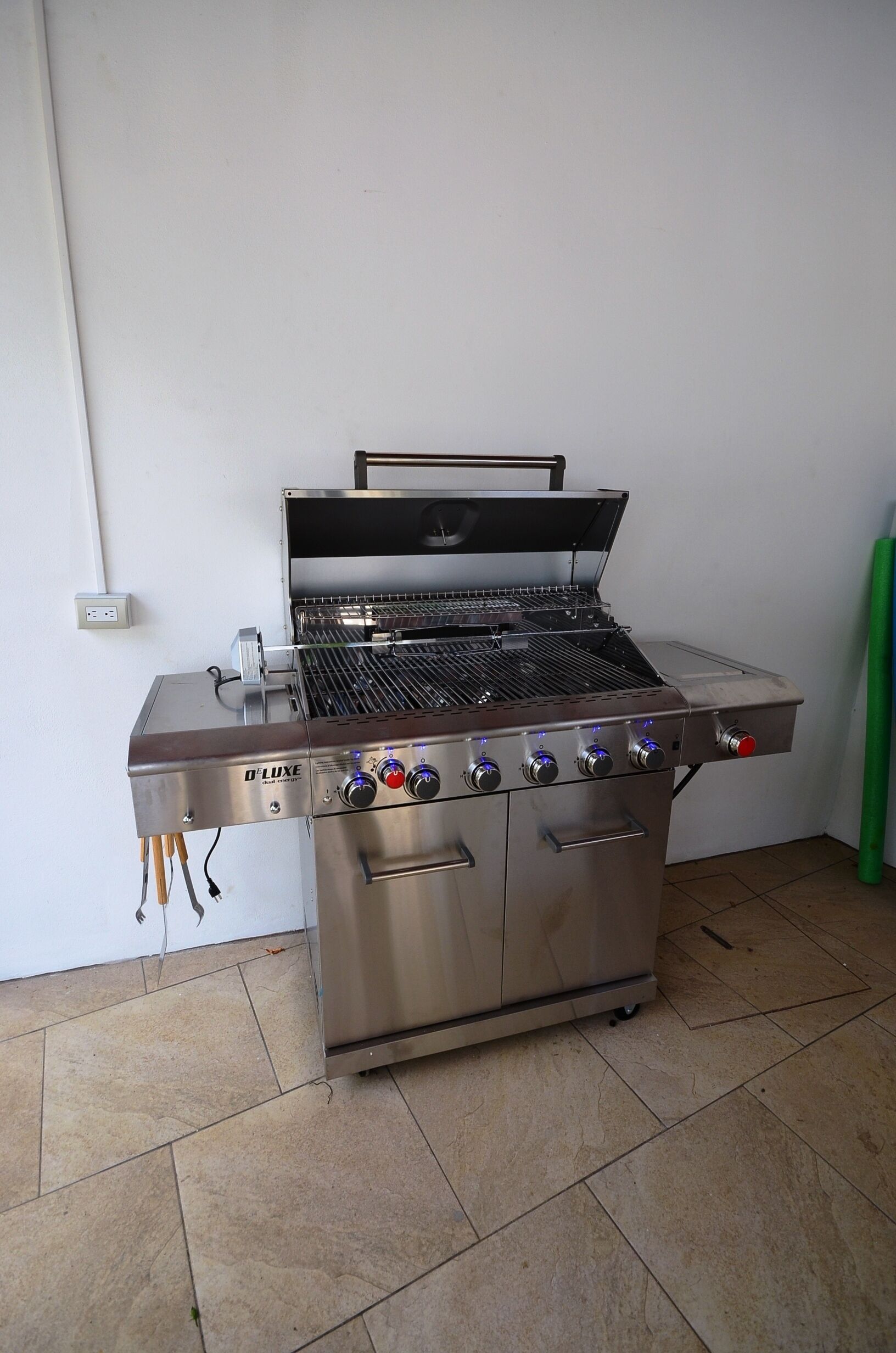 A stainless steel D'Luxe portable grill with a digital control panel, a side burner, and a foldable lid.