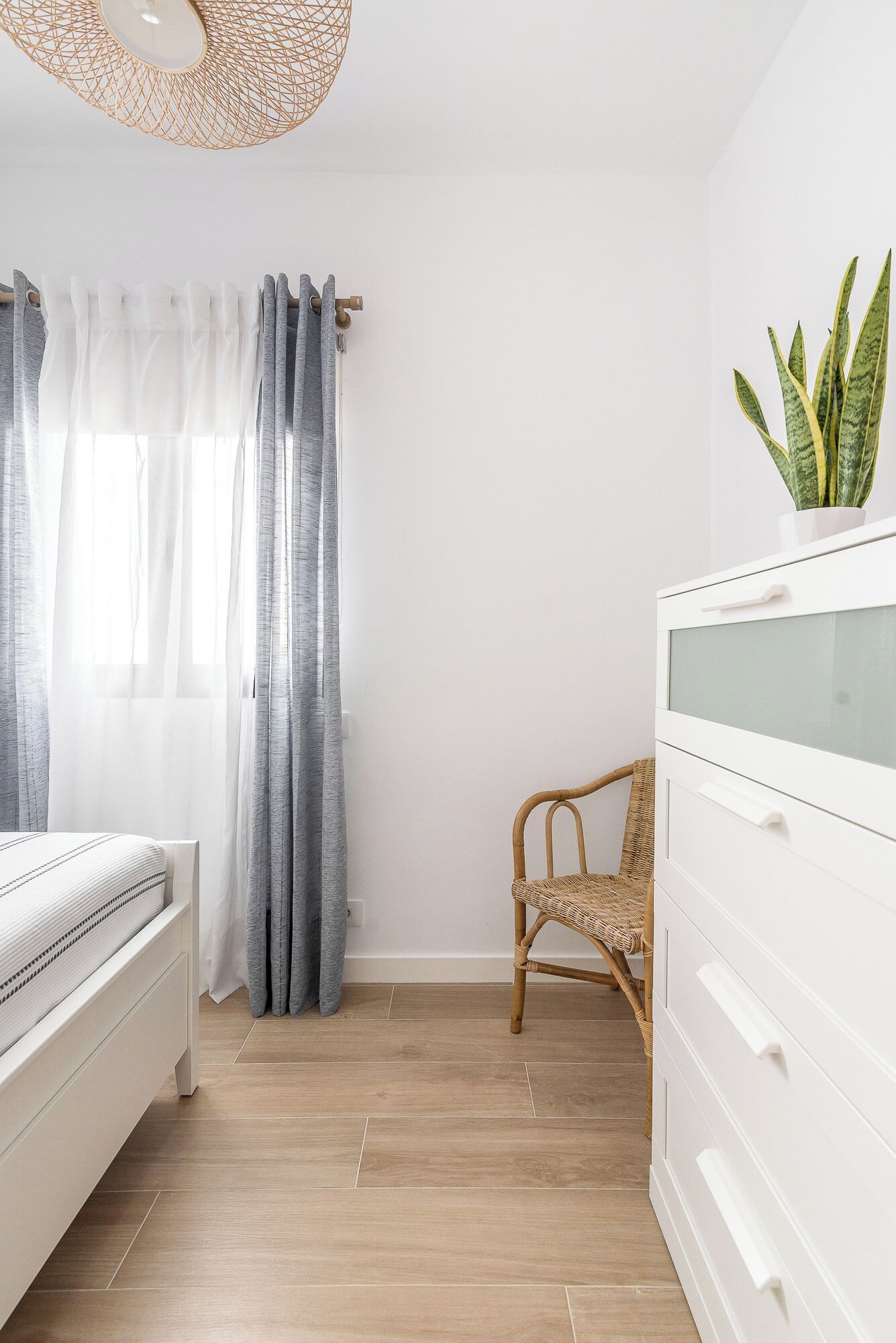 A bedroom with a bed, a dresser, a chair, and a plant.