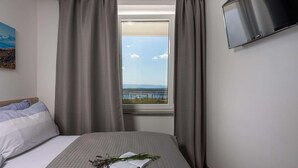 Ein Hotelzimmer mit einem Bett, einem Fenster mit Vorhängen, einem Flachbildfernseher und einem Gemälde an der Wand.