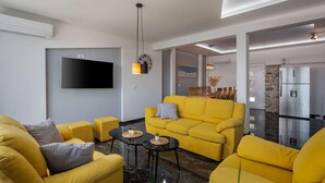 Ein modernes Wohnzimmer mit einem gelben Sofagarnitur, einem Flachbildfernseher und einem Essbereich mit Tisch und Stühlen.