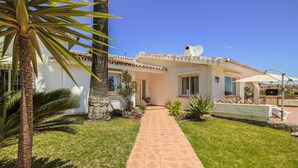 Una villa con un camino empavedado que lleva a la entrada, rodeada de césped cuidado y palmeras.