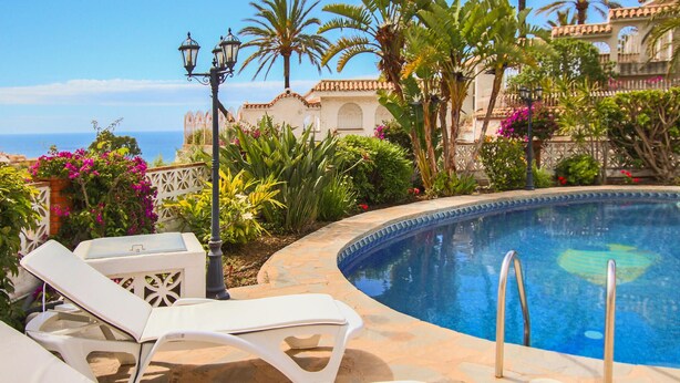 Zona de piscina con sillones de descanso, piscina y vista al mar.