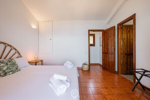 A bedroom with a bed, pillows, a bedside table with a lamp, a wooden door, and a woven basket.