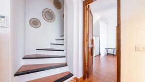 Un escalier aux murs blancs et aux marches marron mène à une pièce dont la porte est en bois.