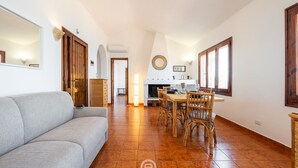 Un grand espace de vie comprenant un canapé, une table à manger avec des chaises, et une cuisine à l’arrière-plan.