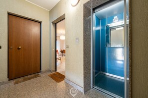 A hotel lobby with a wooden door, a blue elevator, and a welcome mat.