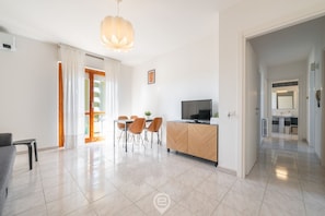A modern living room with a dining area, a TV, and a kitchen in the background.