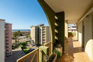 A balcony with a view of a residential area, including a multi-story building and a beach.