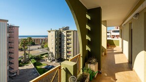 A balcony with a view of a residential area, including a multi-story building and a beach. - Sunset Oasis Apartment (Quartu Sant'Elena)