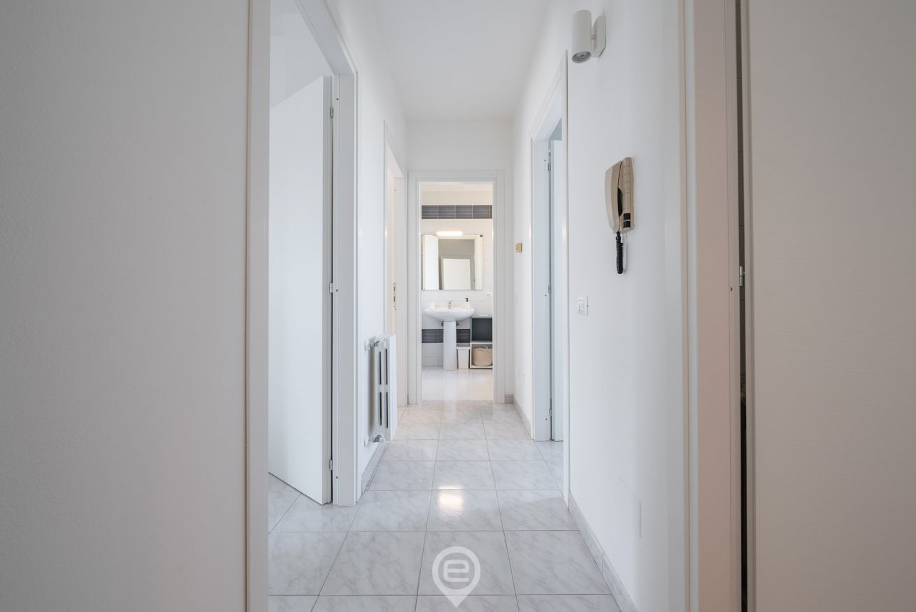 Un pasillo moderno y bien iluminado que conduce a un baño con lavamanos y espejo.