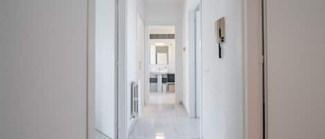 Un pasillo moderno y bien iluminado que conduce a un baño con lavamanos y espejo.