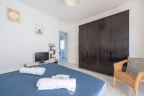 Une chambre à coucher avec un grand lit, une télévision, une armoire et un fauteuil en osier.