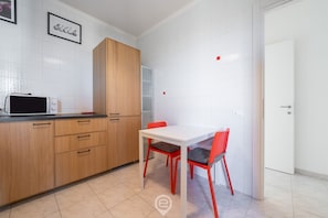 Une cuisine moderne avec des carreaux blancs, un four à micro-ondes, des meubles en bois et une table blanche avec des chaises rouges.