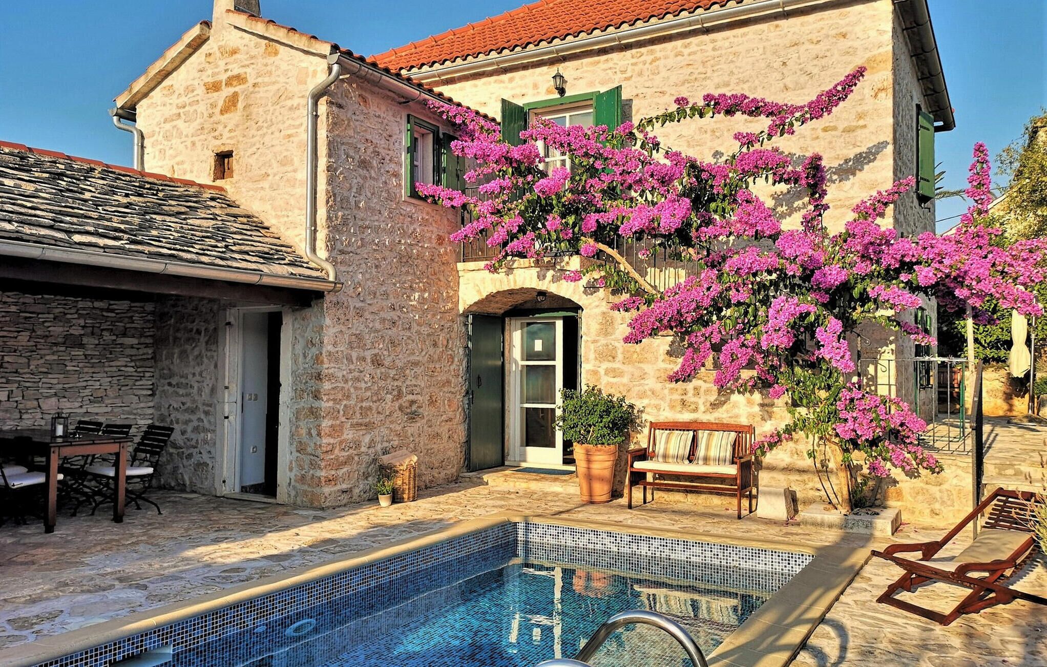 Ein Steinhaus mit Pool, Sitzgelegenheiten im Freien und blühenden rosa Blumen.