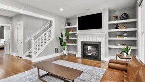 A spacious living room with a fireplace, a television mounted above it, and a staircase leading to another room. - Airport Cottage  (East Point)
