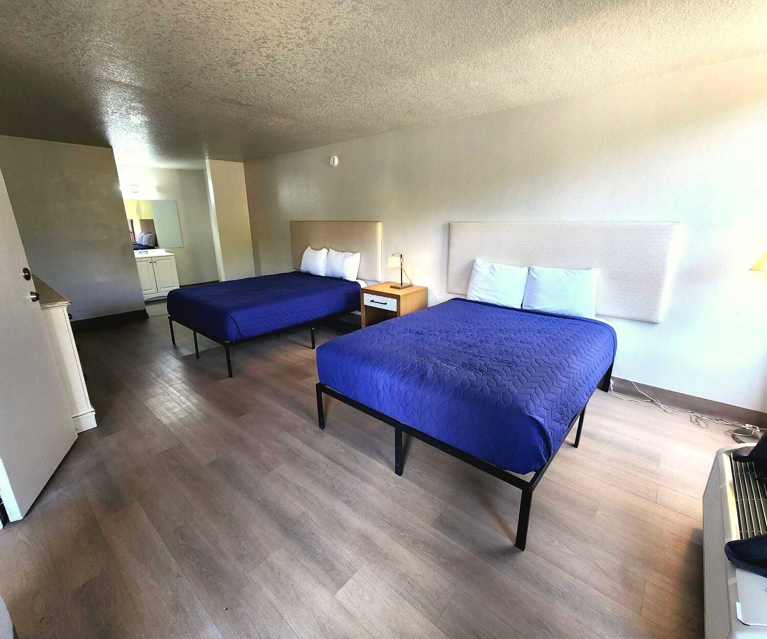 A hotel room with two beds, a desk, a chair, and a small kitchenette.