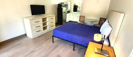 Un dormitorio con cama, cómoda, escritorio con lámpara, televisor, microondas y una mesita.
