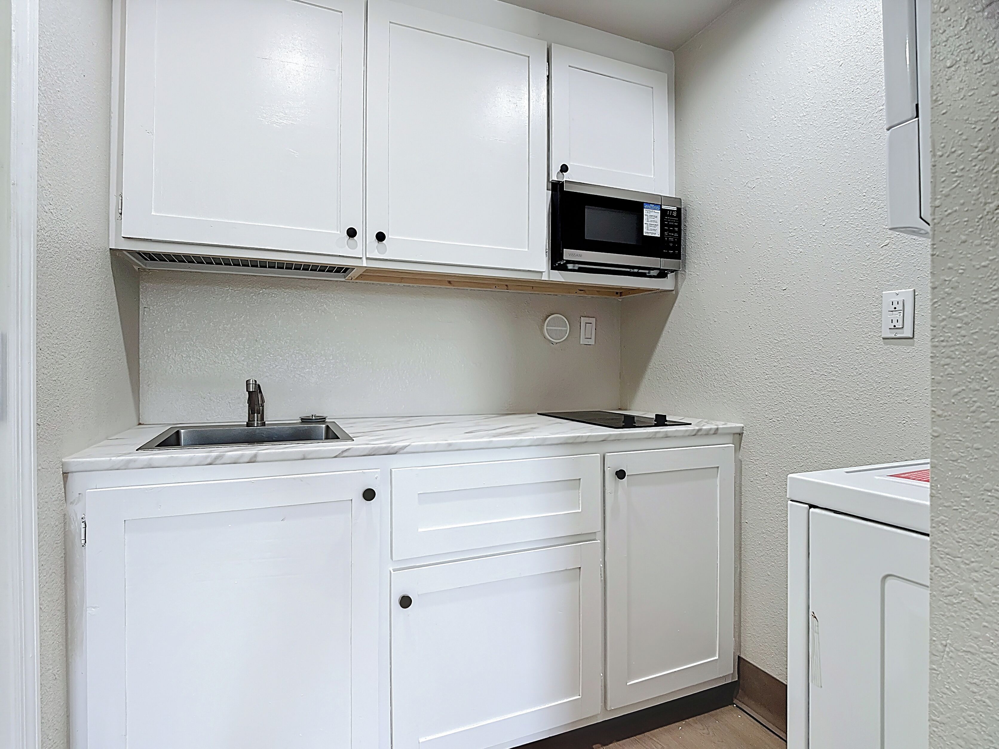 A compact kitchen with white cabinets, a microwave, and a sink.